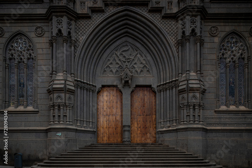 SPAIN, Gran Canaria, Arucas: Vertical View of Neo-Gothic religious architecture charm in the stone facade of San Juan Bautista Church, entrance doors to historic architectural gem in the heart of town