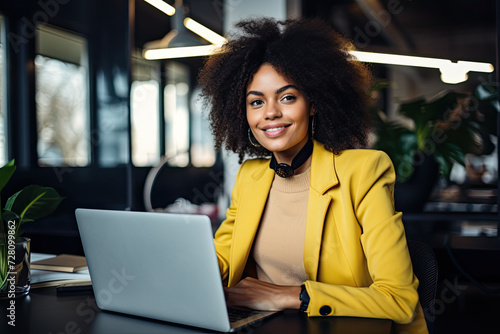 Young happy afro american woman in yellow jacket working on laptop