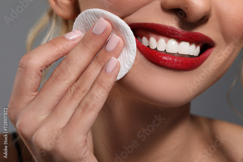 Smiling woman removing makeup with cotton pad on grey background, closeup