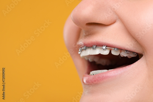 Smiling woman with dental braces on orange background, closeup. Space for text