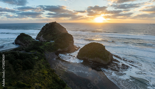 Rough seas, islands and coastline of Bethells Beach at sunset, Auckland, New Zealand.