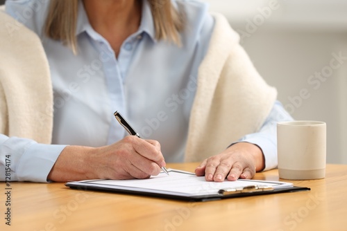 Senior woman signing Last Will and Testament at table indoors, closeup