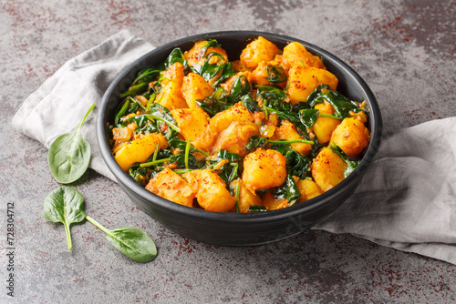 Saag aloo is a classic Indian style side dish featuring potatoes fried in spices and spinach closeup on the bowl on the table. Horizontal
