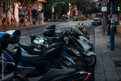 A group of motor scooters parked on the street of a European city in the evening