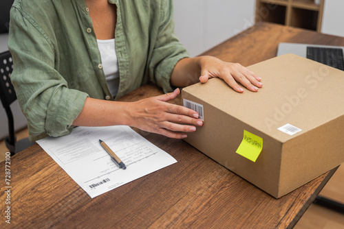 In pursuit of an online shopping refund, a woman places a barcode sticker on a cardboard parcel for return. 
