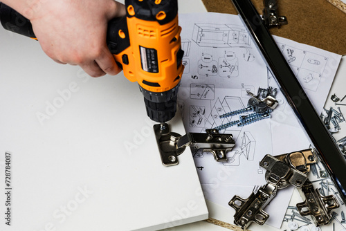 Installing a furniture hinge on the door. Assembling furniture and fixing fittings close-up. Screwing the door hinge onto a piece of furniture with a screwdriver.