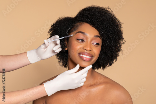 Smiling black woman during cosmetic treatment, beige backdrop