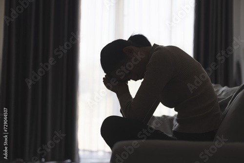 Silhouette of a person suffering from depression in the house, Depressed woman sitting alone on the Sofa feel stress, sad and worried in the dark room. person are stressed.