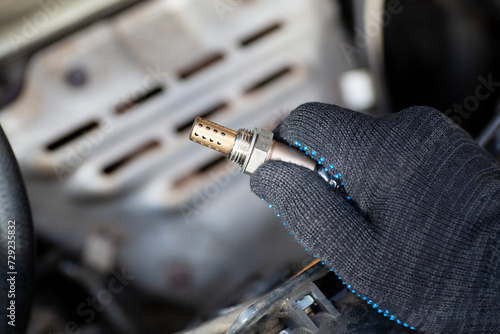 Oxygen sensor for gasoline and diesel engines in the hand against car engine. Mechanic holds oxygen sensor. lambda probe