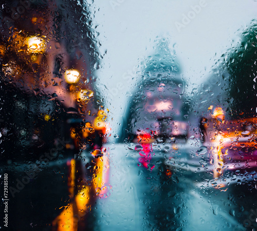 View through a glass window with raindrops on city streets with cars in the rain, bokeh of colorful city lights, night street scene. Focus on raindrops on glass 