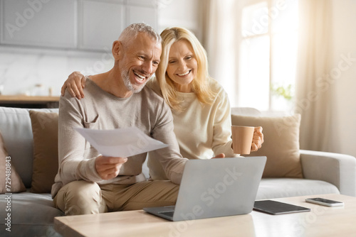 Happy couple of pensioners sitting using computer at home