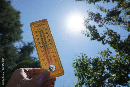 Hand holding thermometer towards the sun and clear sky showing representing raising temperatures and hot weather