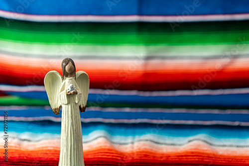 Beautiful angel holding dove figurine with Mexican blanket as backdrop.