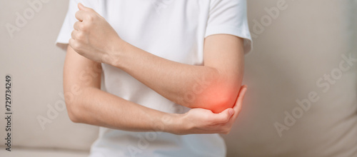 Woman having elbow ache during sitting on couch at home, muscle pain due to lateral epicondylitis or tennis elbow. injury, Health and medical concept