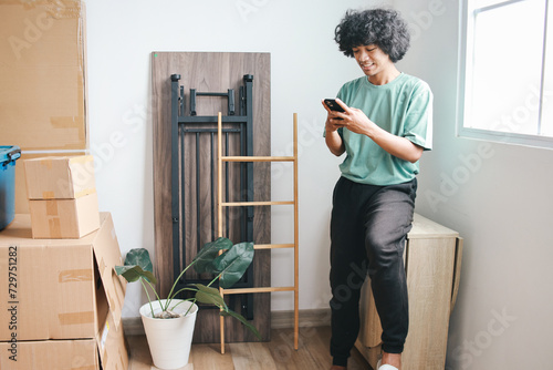 Asian guy with curly hair using smartphone after moving in new house
