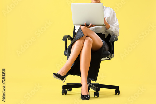 Businesswoman with high heels using laptop in office chair on yellow background