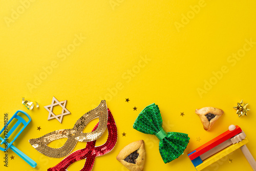 Joyous Purim theme captured from top view, showcasing iconic hamantaschen cookies, Star of David, celebratory accessories like masks, bow tie, ratchets on vibrant yellow backdrop for your message