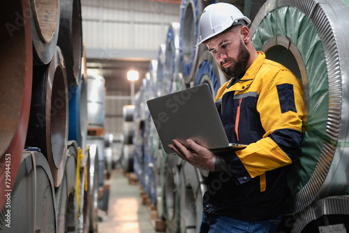 Industrial engineer in safety helmet uniform jacket working in heavy steel engineering factory. Technician manager worker inspector using laptop in metalwork product manufacturing facility workplace