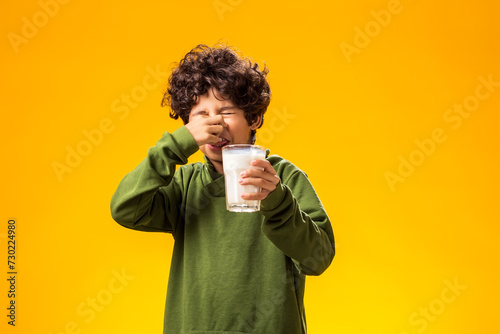 Lactose intolerance. Dairy intolerant child boy holding glass of milk over yellow background.