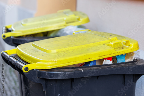 Full recycling plastic yellow packing bins with yellow lids against an urban backdrop, signaling waste management