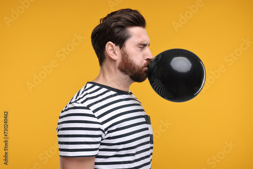 Man inflating black balloon on yellow background