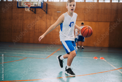 A young basketball kid in action dribbling a ball on court on training.