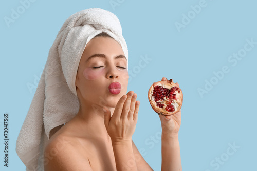 Young woman with under-eye patches and pomegranate blowing kiss on blue background, closeup
