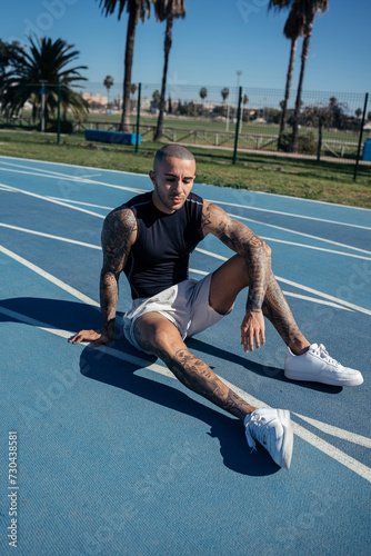 Chico joven musculado y tatuado posando en pista de atletismo con indumentaria deportiva 