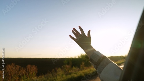 Road trip female hand from window of driving car at sunset sunrise rural summer field closeup. Woman arm enjoy freedom air travel adventure active lifestyle automobile journey exploration discovery