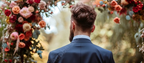 Man, in suit, considering outdoor wedding with floral decorations for celebration and commitment to relationship.