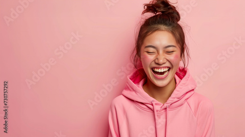 Portrait of cheerful, adult girl with hair gathered in bun. Wearing in T-shirt. Laughing with eyes closed. Stand isolated over pastel color background.