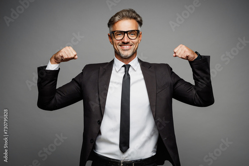 Adult strong happy fun successful employee business man corporate lawyer wear classic formal black suit shirt tie work in office show muscles on hand isolated on plain grey background studio portrait.