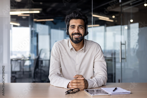 Portrait of a smiling Muslim man businessman, marketer, salesman sitting in the office at the table in a headset and smiling confidently at the camera