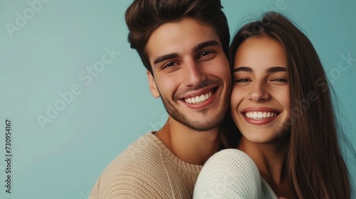 A young couple sharing a joyful moment bracing each other with smiles on their faces set against a soft blue background.