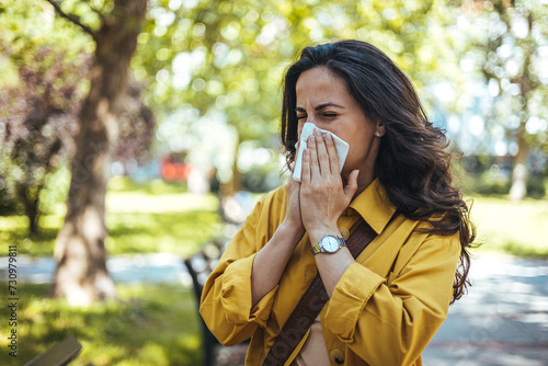 Portrait of unhealthy cute female in yellow top with napkin blowing nose, looks to the source of the allergy, place for advertising. Rhinitis, cold, allergy concept. Pollen allergy symptoms