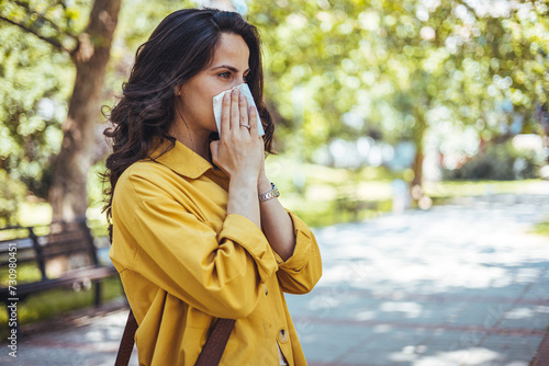 Portrait of unhealthy cute female in yellow top with napkin blowing nose, looks to the source of the allergy, place for advertising. Rhinitis, cold, allergy concept. Pollen allergy symptoms