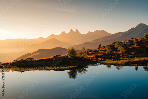 Golden sunrise over Arves massif with lonely tree relfection on Lac Guichard at French Alps