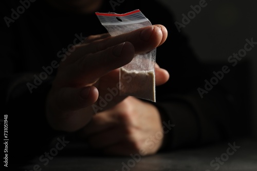 Drug addiction. Man with plastic bag of cocaine at dark table,selective focus