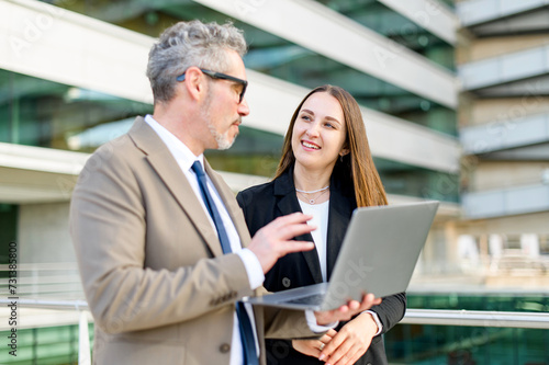 A grey-haired senior businessman communicates with a young female colleague over a laptop, their expressions reflecting a focused business discussion and generational synergy