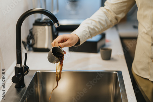 A female figure pours out her distasteful coffee in the sink in the kitchen.