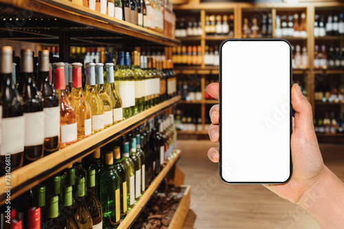 Smart phone with empty screen in female's hand in front of liquor store. Online ordering and shopping of alcohol drinks. Mockup for mobile app.