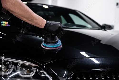 Car detailing worker polishing black car body with electric polisher