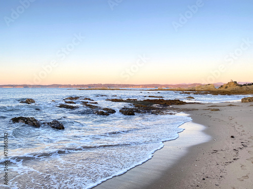 Sunrise on a beach. Dawn on the ocean at low tide. Waves curling on the rocky shore in the morning. Mountain in the distance. Beach at sunset.