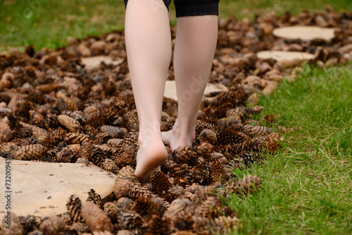 Woman walks barefoot along a massage tactile eco-path made of pine cones. Barefoot path with different textures in the park, foot massage.