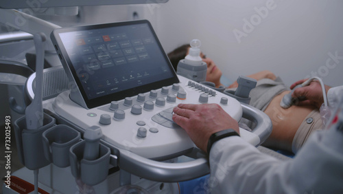 Close up of doctor using sonography machine with digital monitor. Medical specialist does ultrasound diagnostic to pregnant female patient. Modern clinic or medical center with advanced equipment.
