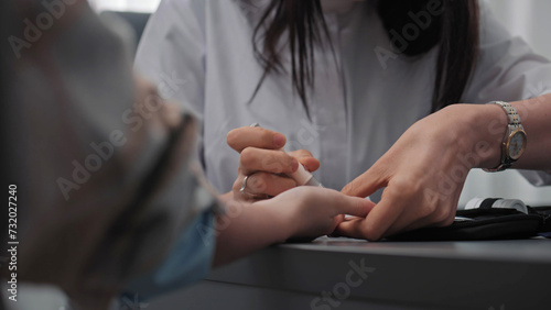 Close up shot of female doctor, nurse taking blood test from finger of patient in hospital using modern lancet device. Medical examination or checkup in clinic. Concept of medicine and healthcare.