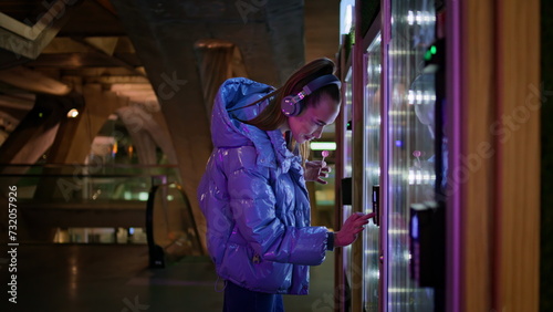 Woman buying snacks vending machine at subway late evening. Girl make purchase.