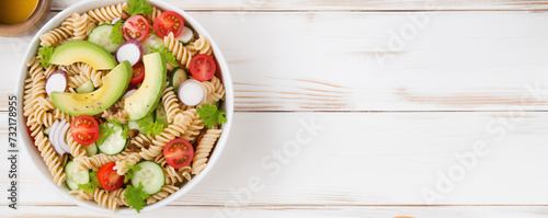 From above, a white bowl holds a delicious Chicken Pasta Salad adorned with avocado, tomato, and dressed with olive oil and vinegar on a white wood table. A visually appealing image, ideal for creativ