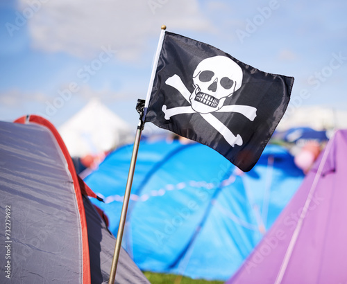 Pirate flag, tent and camping at festival outdoor in summer for party, event or celebration closeup. Skull, crossbones or jolly roger in nature for performance, entertainment or adventure with crowd
