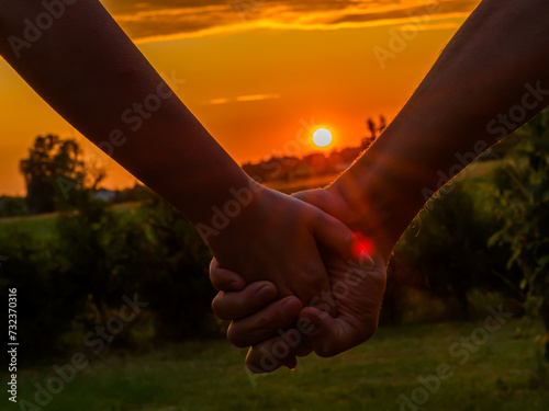 Para trzymająca się za dłonie przy zachodzie słońca, promienie padają na ich złączone ręce 